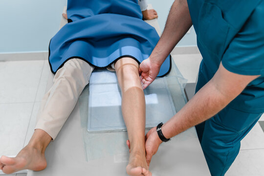 Male doctor works with an x-ray machine in a modern hospital while patient lies on special couch. Radiologist takes a picture of the leg. The concept of medical technologies, modern medical equipment.