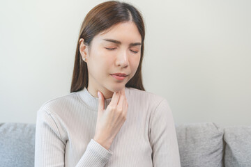 Sickness in inflaming asian young woman, girl use hand check self touch at sore throat, pain thyroid gland on neck or disease reflux, acid of suffer people on wall background. Medical and healthcare.