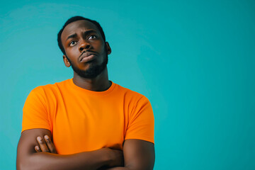 Fototapeta premium Portrait of a confused puzzled minded African American man in orange top isolated on blue background, with copy space.