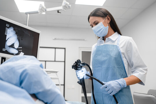 Female doctor holding modern endoscope device before gastroscopy examination. Gastroenterologist with probe to perform colonoscope in white lab coat protective gloves and facial mask