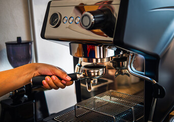 Hand of barista holding portable coffee filter handle to prepare making an espresso coffee in coffee shop