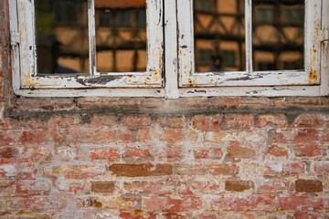 Old shabby house wall made of brick with rusty white window. Vintage background.