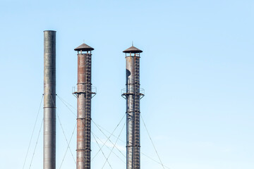 Old metal industrial pipes with ladders and blue cloudless sky.