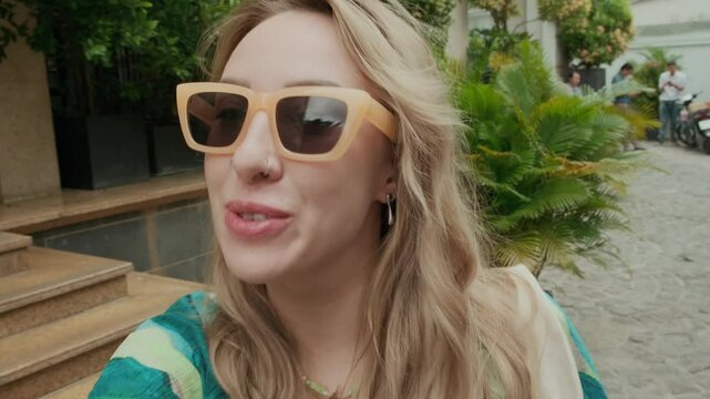 Handheld selfie shot of young Caucasian woman in orange sunglasses filming vlog about her summer vacation, UGC