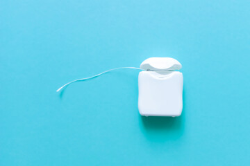Dental floss in white plastic packaging. Blue background.
