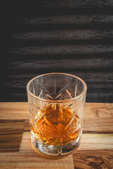A beautiful glass of wiskey, on a black background, and a wooden table.