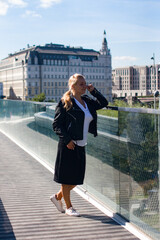 A beautiful stylish woman in a leather jacket walks in the park. Blonde