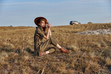 Woman in a hat enjoying a peaceful moment in the middle of a field with a car in the background