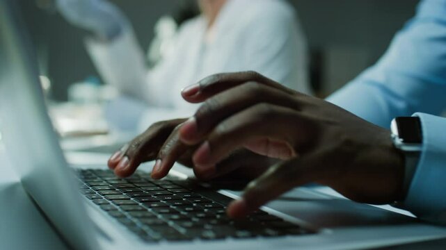 Close up view of hands of unrecognizable Black investigator typing on laptop at desk in crime lab, forensic scientist working in background