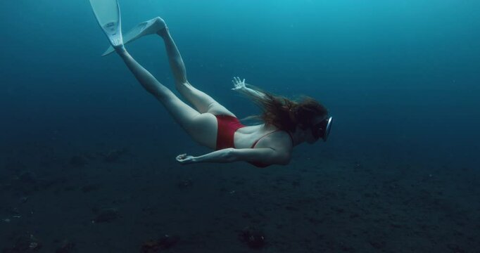 Woman with vintage mask glides underwater with fins on deep blue ocean. Free diving of beauty woman in transparent sea