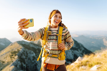 Young woman enjoying a hiking adventure while taking a selfie on a mountain summit during a sunny day. Nature freedom adventure, happy vacation. Blogging. © maxbelchenko