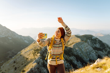 Young woman enjoying a hiking adventure while taking a selfie on a mountain summit during a sunny...