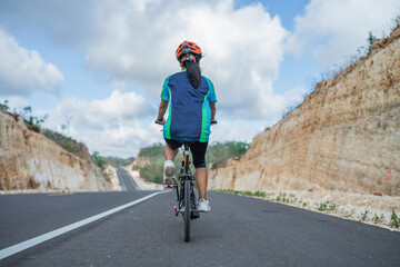 Obraz premium rear view female biker enjoying riding bike on the road, between cliff