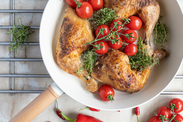 Baked chicken legs with cherry tomatoes and fresh thyme in a frying pan on light kitchen counter background