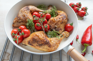 Baked chicken legs with cherry tomatoes and fresh thyme in a frying pan on light kitchen counter background