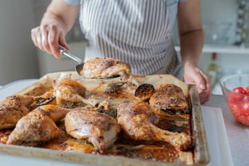 Woman with apron serving fresh and homemade cooked roast chicken legs on a baking tray in the kitchen