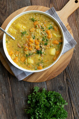 Healthy green lentil soup with bacon, cabbage, potatoes, and carrots on a deep plate on wooden table background