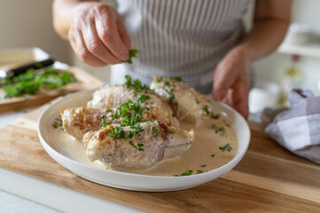 Woman sprinkling chopped parsley over a fresh and homemade cooked dinner with turkey roulades in a cream sauce.