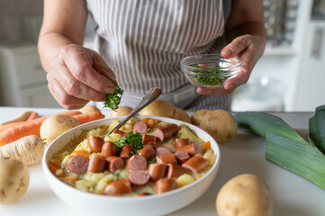 Woman garnishing fresh and homemade cooked potato soup with vienna sausage in the kitchen