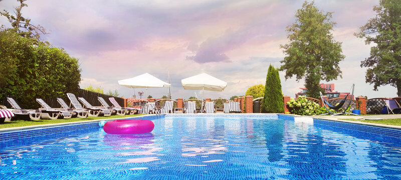 Swimming pool with sunbed around outdoor water in hotel resort. Beach accessories (pink inflatable ring) float on water. Sunset view..
