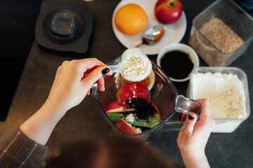 Close up top view woman adding plant based pea protein powder during making smoothie on the...