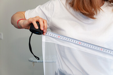 Girl in white t-shirt construction roulette measures the width of the curtains.