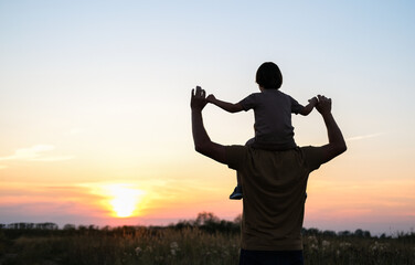Silhouette of a father with a child on his shoulders against the sunset sky