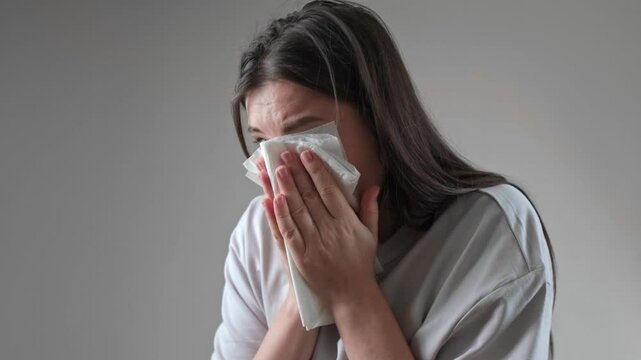 Using a tissue to clean the nose, with nasal moisturizing and cleansing products nearby for sinus care.