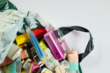 Discarded and broken vapes falling out of a plastic bag. Shot against a white paper background with...