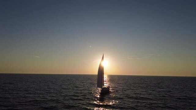 forward low aerial drone 4K film of sailboat yacht sailing on sea ocean water with Dutch holland flag at sunrise sunset silhouette