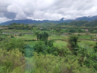 Scenic view of lush green valley with mountains under cloudy sky, captured in rural landscape.