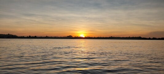 Obraz premium Stunning sunset over a calm lake with a mix of colorful skies and serene water, capturing the beauty of nature's evening display.
