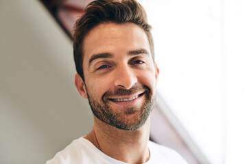 Portrait, morning and happy man in hotel to relax with leisure and healthy energy in home or apartment. Confidence, face and male person with smile in house bedroom to wakeup, rest or break in Spain