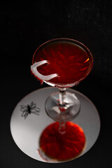 Vampire's Kiss Cocktail. Dracula's Blood Cocktail or Mocktail on dark background with reflection in mirror. Drink for Halloween with plastic vampire teeth as a garnish. Festive food and beverages.