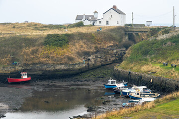 Fototapeta premium Tidal harbour in England with low mud port and small fishing vessel ships run aground waiting for high tide along the beach in grey weather, long exposure image