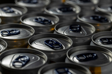 Close-up view of several aluminum beverage cans arranged in rows. The cans feature dark blue pull tabs and a metallic sheen, with soft lighting emphasizing the smooth surfaces