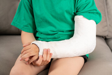 A child's arm is broken.Child with a fractured limb outdoors. fracture injury in the summer holiday. Kid is moving fingers in plaster cast on the arm