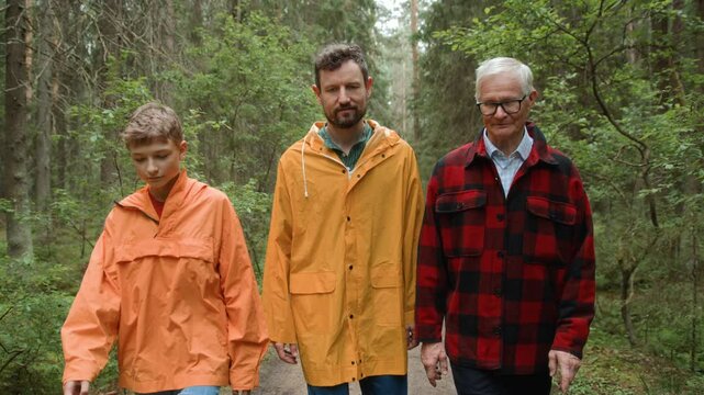 Grandfather, son and teenager grandson walk together along pathway in forest. Three male family generations enjoying bonding together, communication and strolling. Elderly and adult man, and teen boy