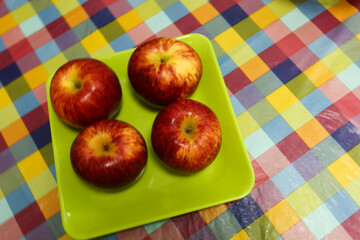 close up of four red fresh apples on a green plate on a colourful table cloth