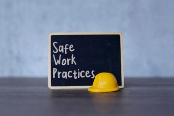 Small chalkboard with the text “Safe Work Practices” and yellow hard hat. Concepts of safety,...