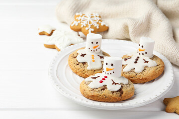 Delicious cookies with snowmen made of marshmallows on white table, closeup