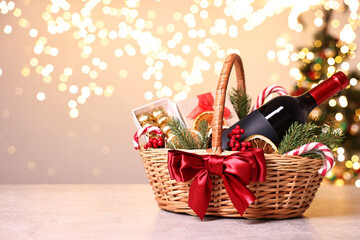 Wicker gift basket with wine and Christmas decor on light textured table, space for text