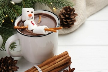 Funny snowman made with marshmallows in cup of hot chocolate and winter decor on white table