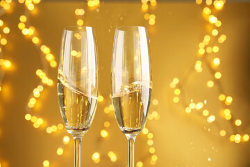Glasses of sparkling wine against golden background with blurred lights, closeup. Christmas decor