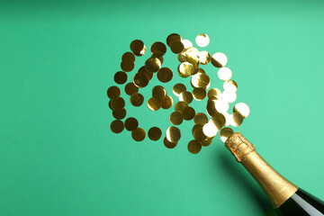 Bottle of sparkling wine and confetti on green background, flat lay with space for text. Christmas decor