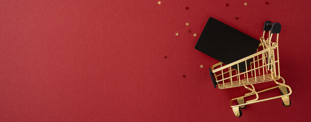 Golden shopping cart with a gift card on a festive red background. Represents Black Friday and...
