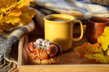 Yellow mug with warm coffee, tea, and cinnamon bun. Autumn time.