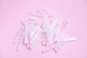 Medical eye drops in plastic pipettes on pink background. Pile of empty plastic ampoules for drops....