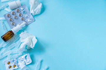 Medicines and pills background. Season of colds and illnesses. Treatment concept. Nasal spray for runny nose and crumpled paper tissues on blue background. Copy space