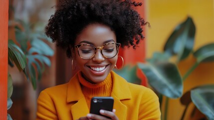 Stylish woman in orange coat using phone on colorful street